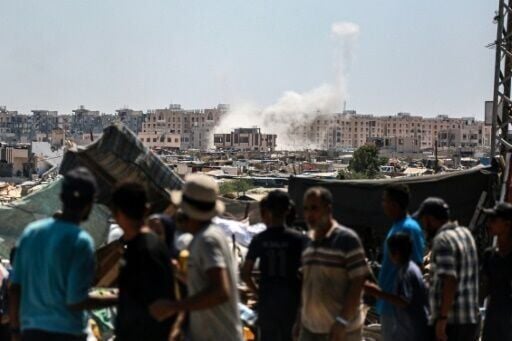 Displaced Palestinians watch from a makeshift camp as Israeli shelling hits Khan Yunis in the southern Gaza Strip